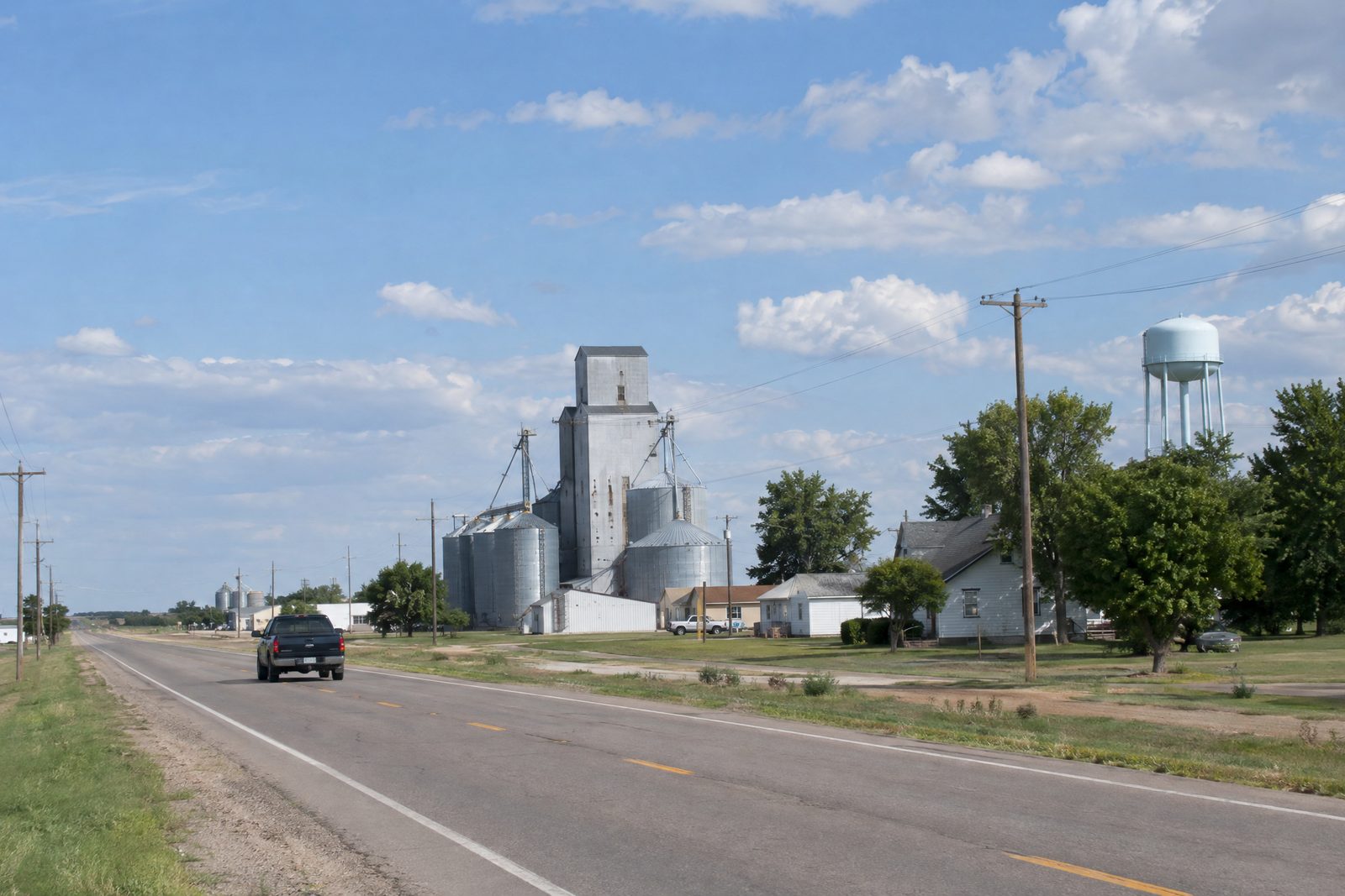 A two-lane highway passing a small plains town with a grain elevator