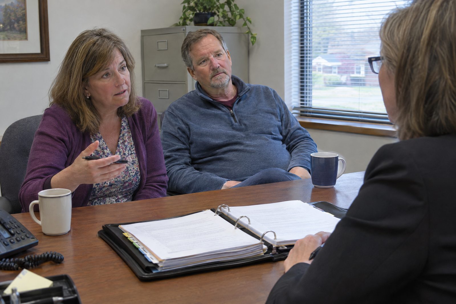 A couple in their fifties going through a binder of trust documents with their attorney