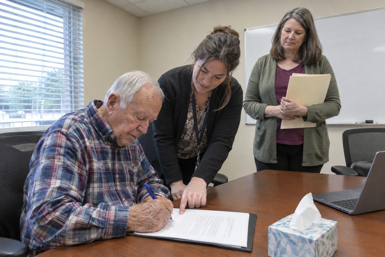 An older man signing papers at a law office table while a paralegal points to the signature line